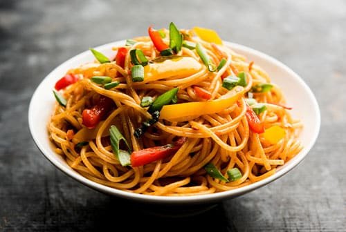 A bowl of steaming hot noodles with chicken, vegetables, and peanuts, garnished with cilantro and lime. A delicious and spicy main course in Indian and Thai cuisine.